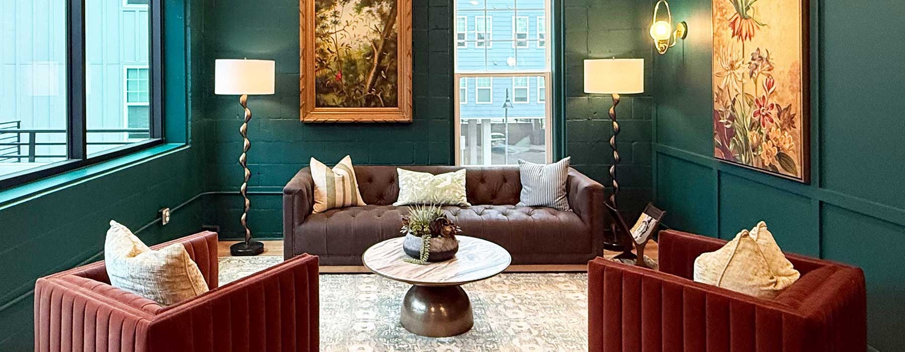 A seating area with couch, chairs, lamps and green walls with a coffee table.